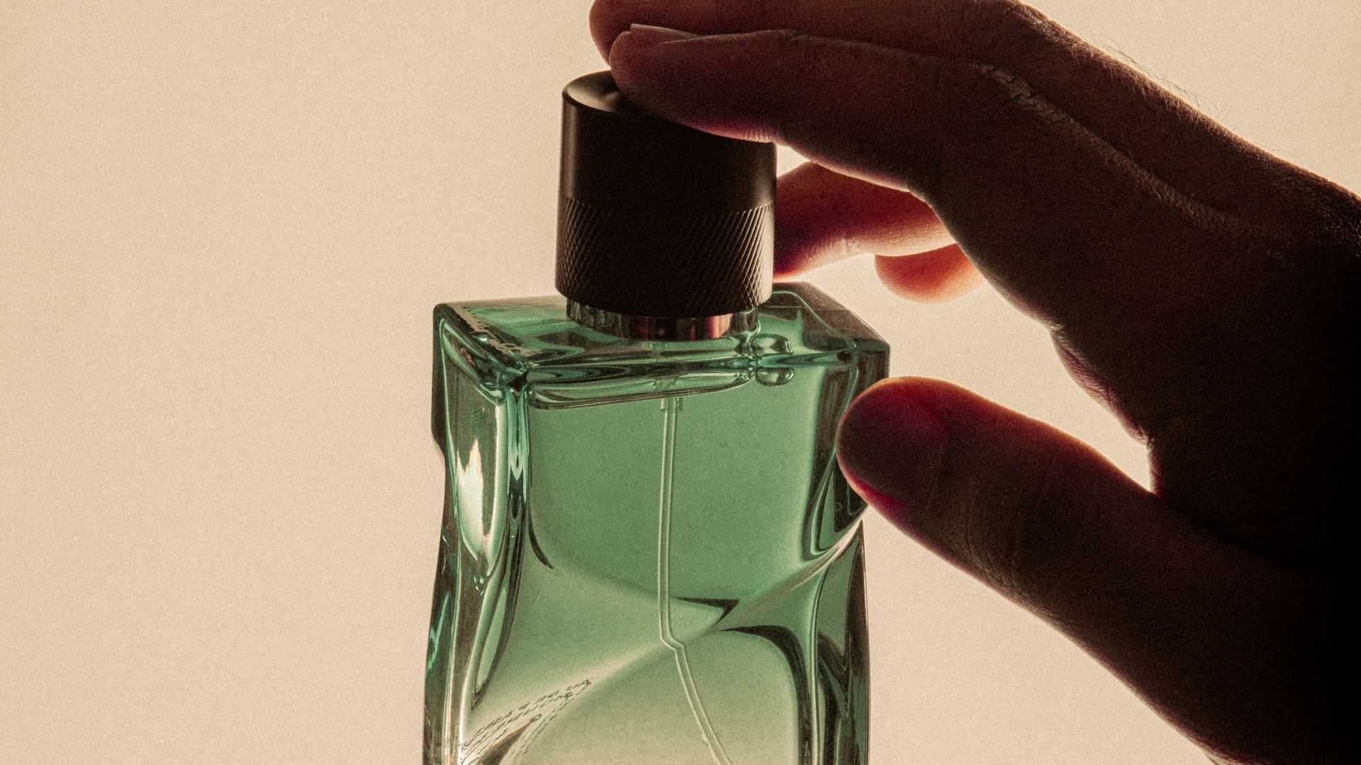 Dłoń trzymająca zielony flakon perfum